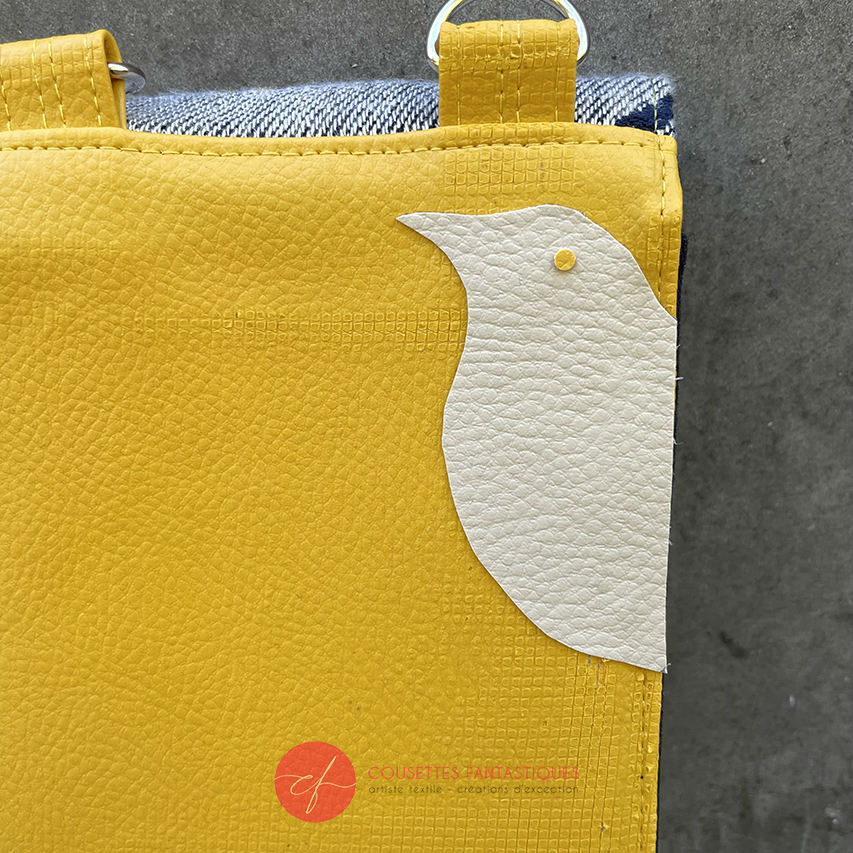 A phone-purse made from a gray, navy blue, and yellow babywearing scarf with bird motifs, and sun-yellow faux leather.