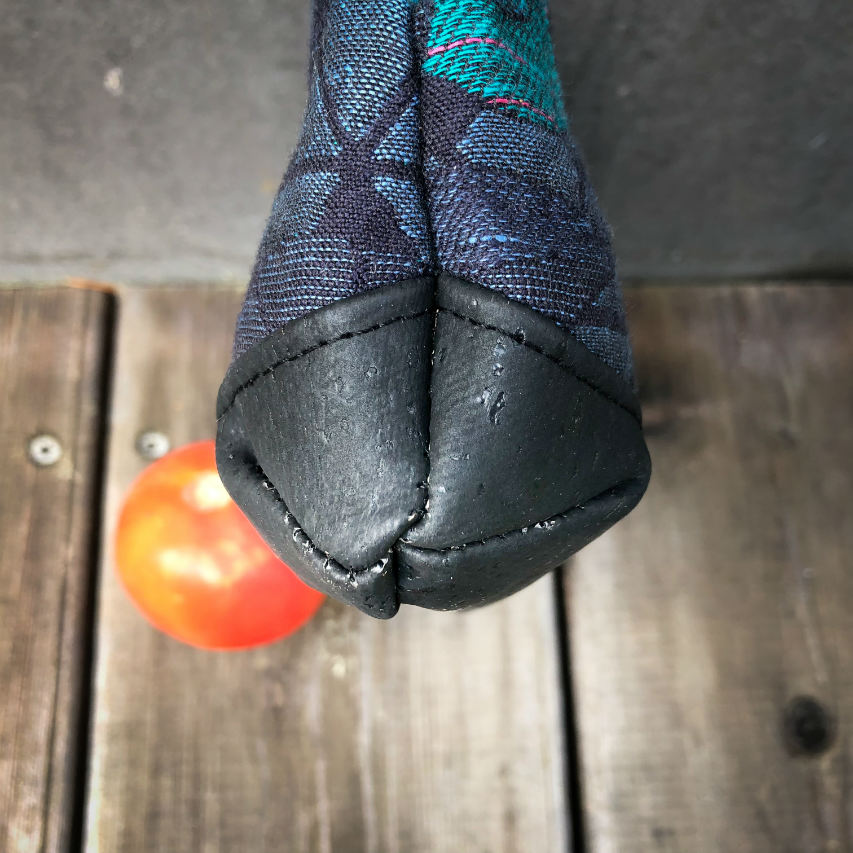 A small zippered clutch sewn in black cork and a babywearing wrap with geometric and floral patterns in shades of blue, green, and pink.