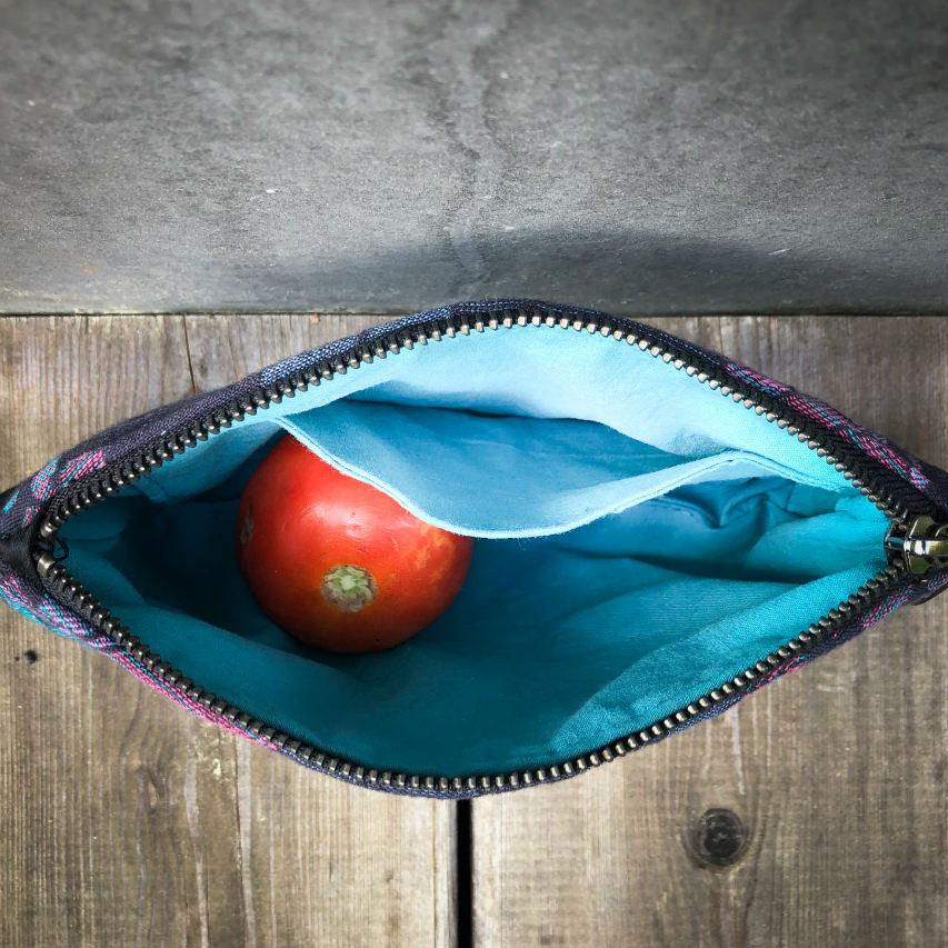 A small zippered clutch sewn in black cork and a babywearing wrap with geometric and floral patterns in shades of blue, green, and pink.