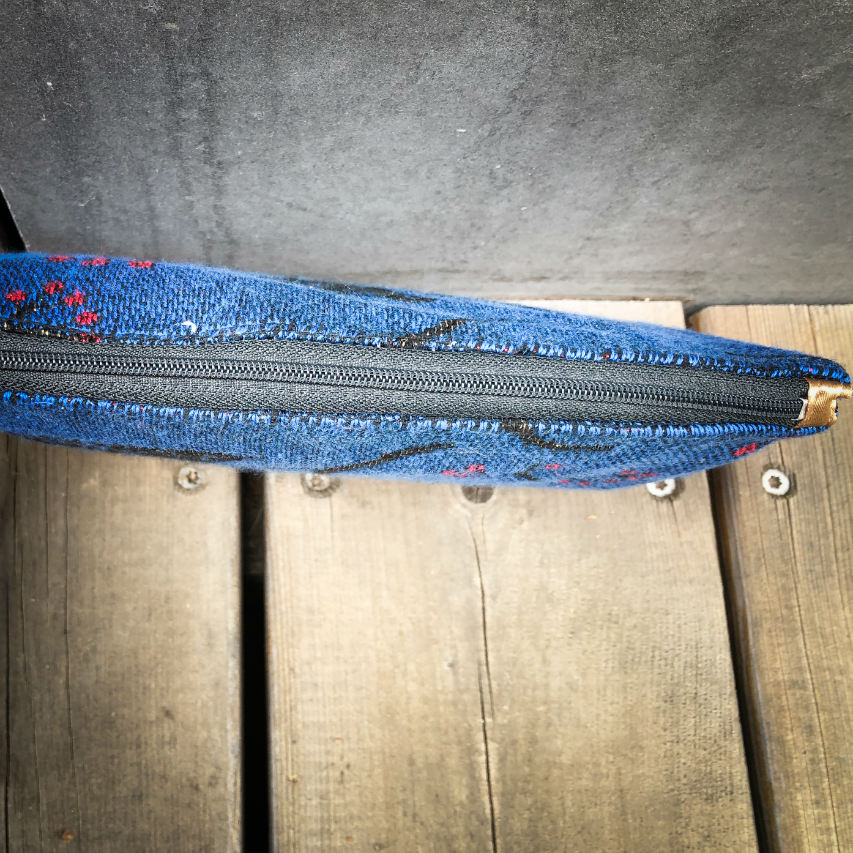 A small zippered clutch sewn in orange leather and a babywearing wrap in electric blue, black, and red with a motif of birds in branches.