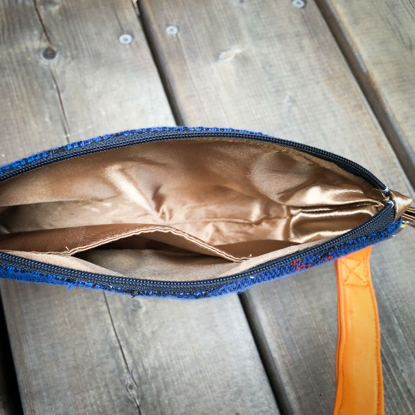 A small zippered clutch sewn in orange leather and a babywearing wrap in electric blue, black, and red with a motif of birds in branches.