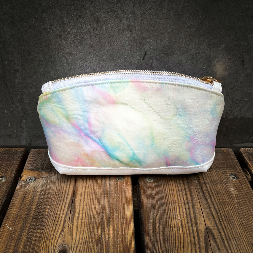 A small zippered pouch made of white faux leather and a hand-painted silk scarf.