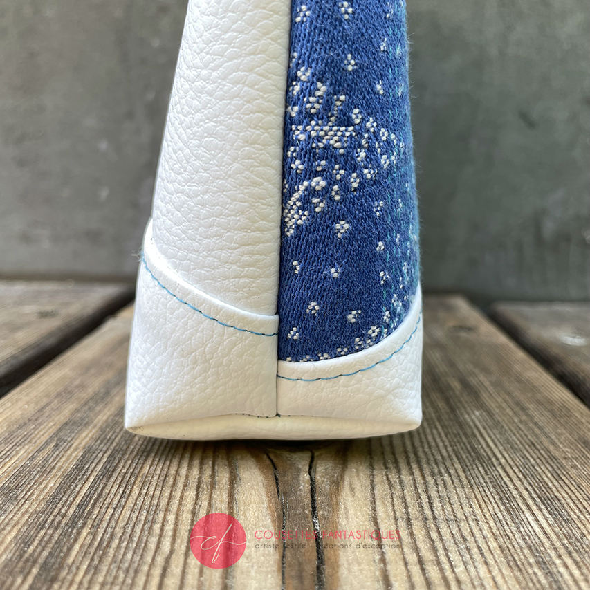 A small zippered pouch made of blue and white babywearing wrap with pointillist star motif and white faux leather.