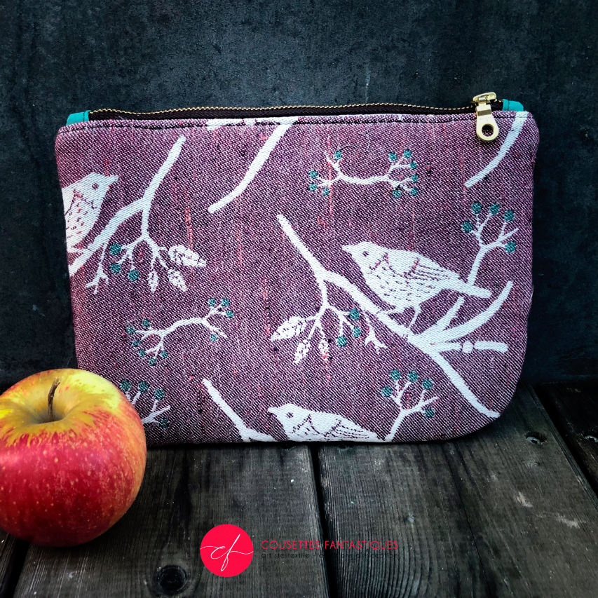 A zippered pouch sewn from a mauve and green babywearing wrap with a bird motif on branches, combined with emerald green cork.