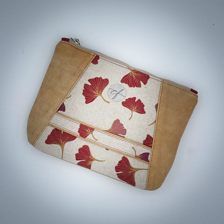 A zippered pouch sewn from a camel colored leather and a red Ginkgo Biloba leaves patterned polycotton canvas.