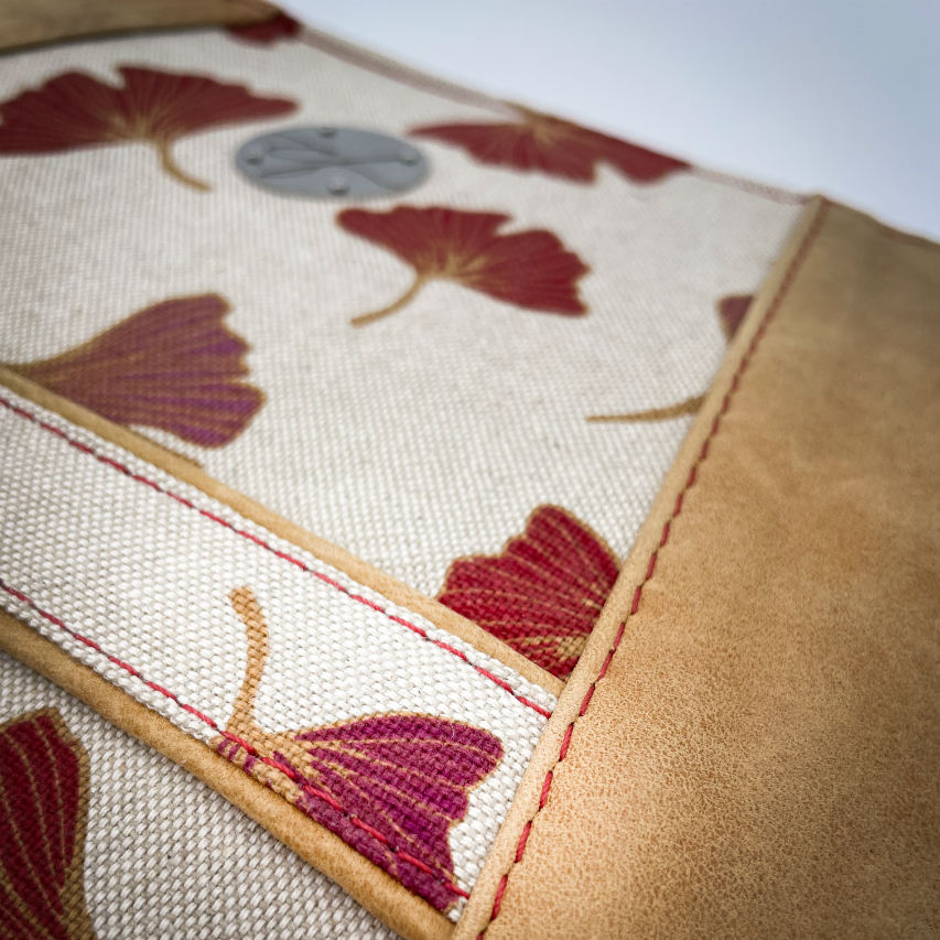 A zippered pouch sewn from a camel colored leather and a red Ginkgo Biloba leaves patterned polycotton canvas.