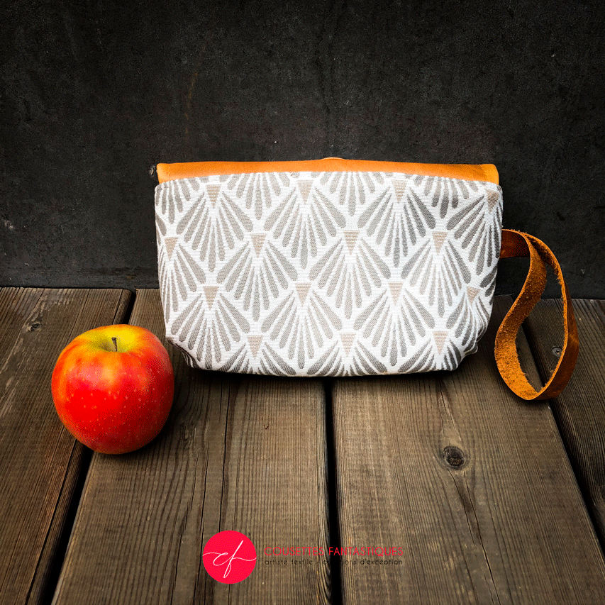 A flap clutch sewn in caramel leather, white damask, and vintage beige and gray patterned fabric, lined with taupe canvas.