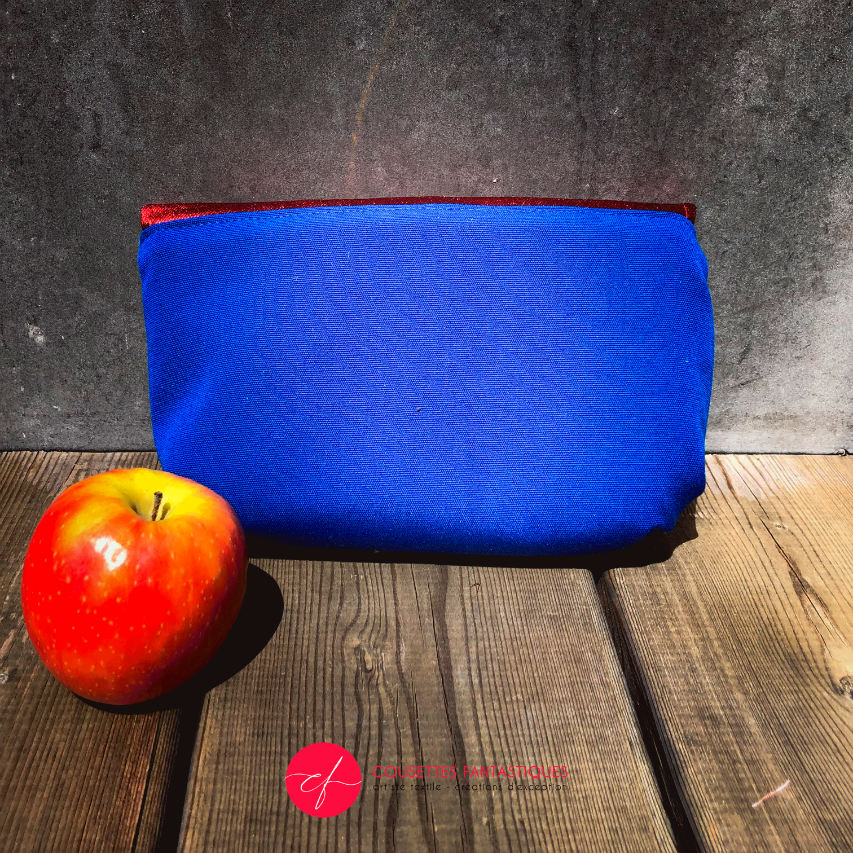 A small flap clutch sewn in blue canvas, metallic red-coated denim, and a glittery avian patterned babywearing wrap, lined with golden satin.