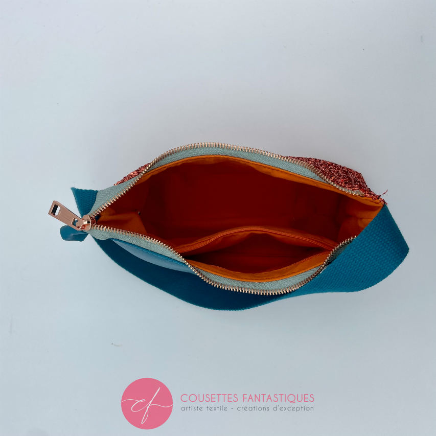 A zippered small shoulder bag made from stretch fabric with copper metallic bouclé, turquoise blue faux leather, and bright light orange lining.