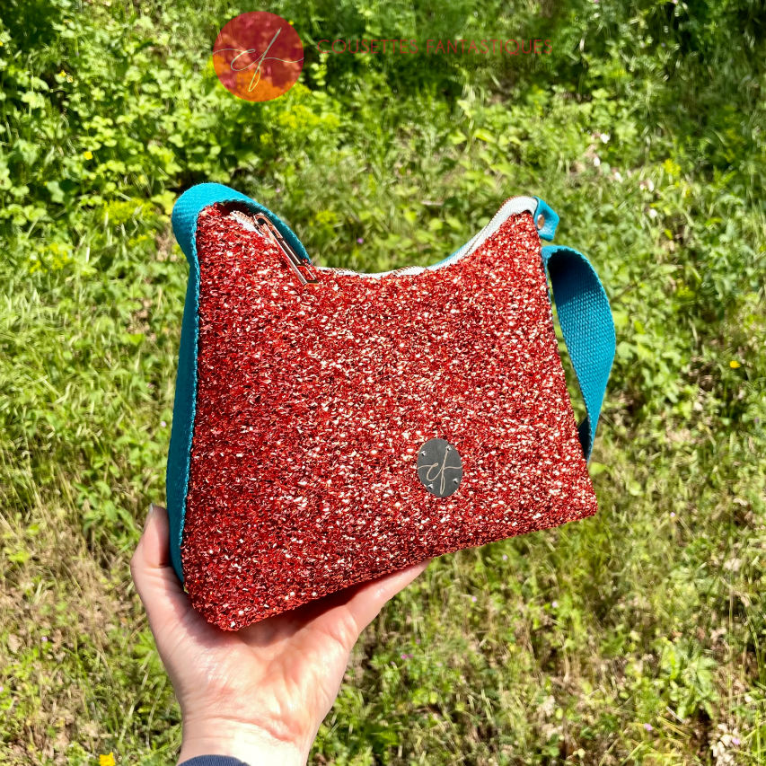A zippered small shoulder bag made from stretch fabric with copper metallic bouclé, turquoise blue faux leather, and bright light orange lining.