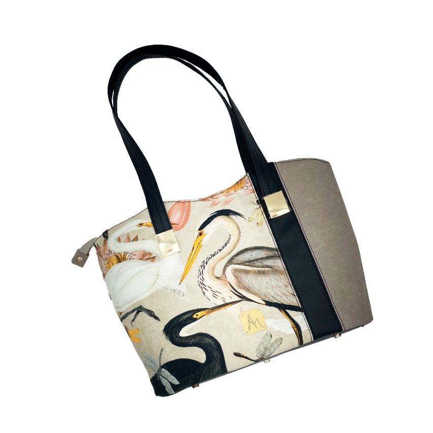 A large zippered shoulder bag, reminiscent of a tote, made from a thick fabric with a wild bird pattern, combined with black and taupe faux leather, and lined with mottled cream linen and coral.