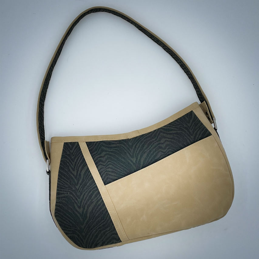 A shoulder bag made from a fabric with the pattern and texture of a forest green tiger fur paired with beige suede-like faux leather, and a lining composed of a high-fashion viscose with very small green and white gingham checks and a cream mottled linen sheet.