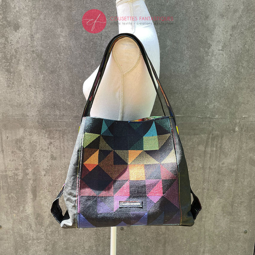 A shoulder bag made from black and rainbow geometric-patterned babywearing scarf and black cork, with a bright rainbow swirl interior.