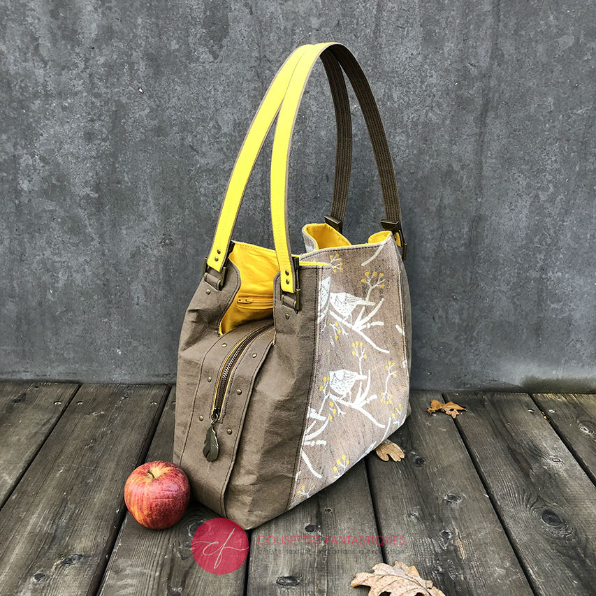 A shoulder bag made from black and rainbow geometric-patterned babywearing scarf and black cork, with a bright rainbow swirl interior.