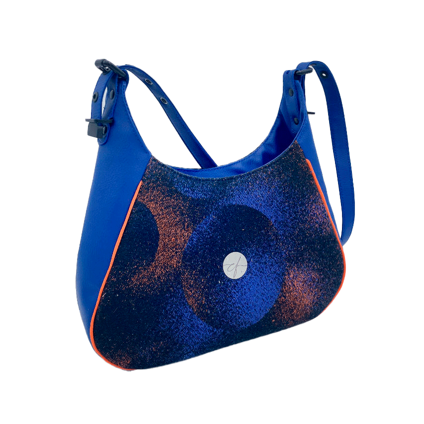 A zippered shoulder bag made from black, blue, pink and orange babywearing wrap scrap, royal blue faux leather, and bright light orange lining.