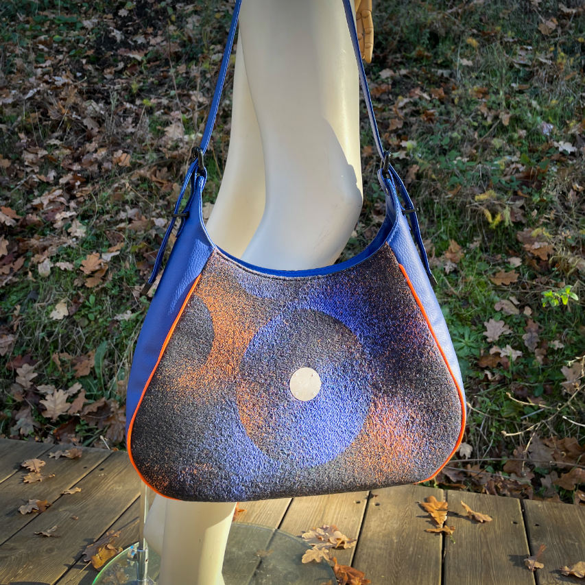 A zippered shoulder bag made from black, blue, pink and orange babywearing wrap scrap, royal blue faux leather, and bright light orange lining.