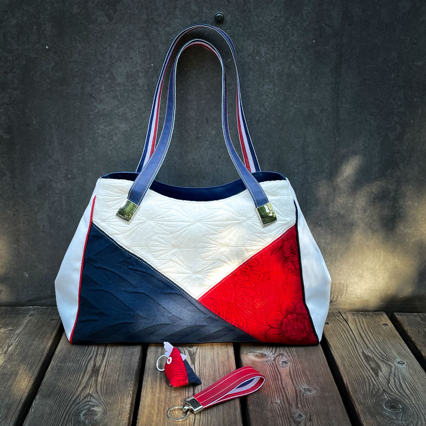 A shoulder bag made with several babywearing wrap coupons (blue, white, and red) and white and blue faux leather.