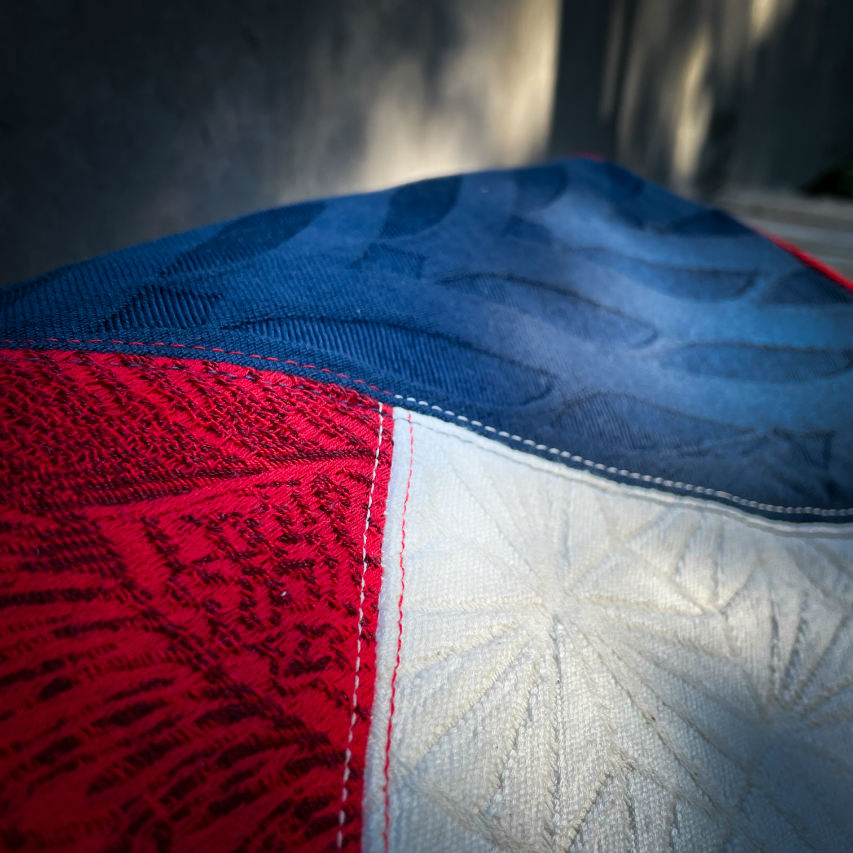 A shoulder bag made with several babywearing wrap coupons (blue, white, and red) and white and blue faux leather.