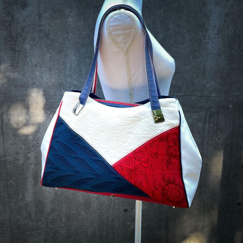 A shoulder bag made with several babywearing wrap coupons (blue, white, and red) and white and blue faux leather.