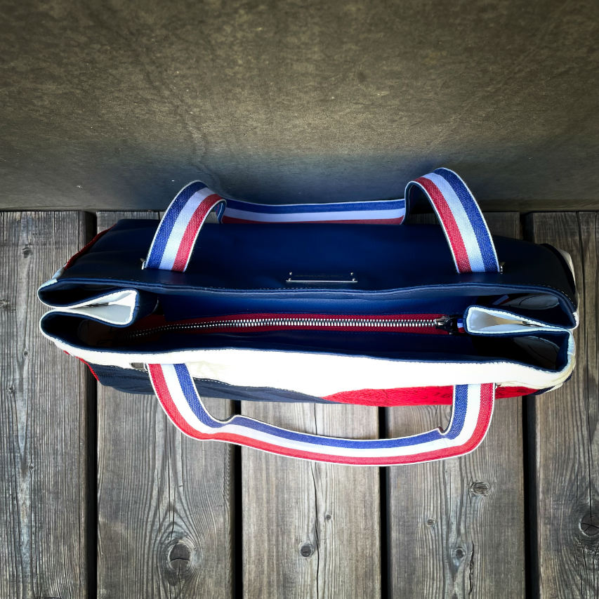 A shoulder bag made with several babywearing wrap coupons (blue, white, and red) and white and blue faux leather.