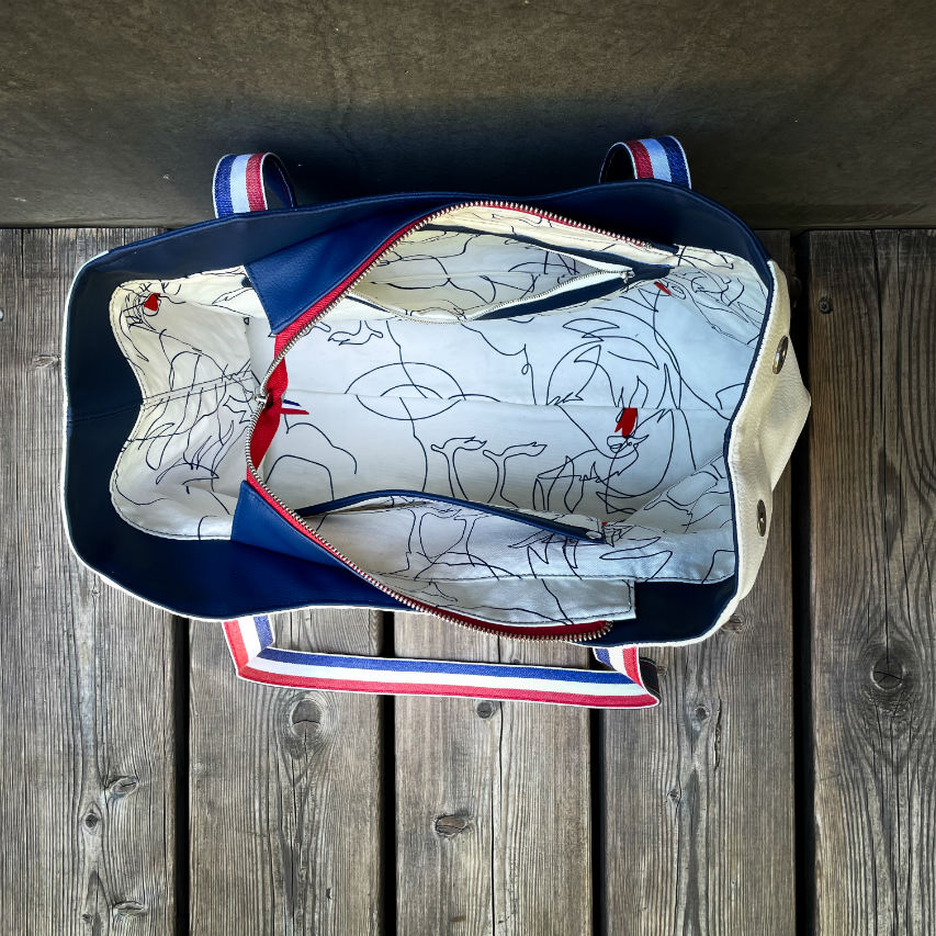 A shoulder bag made with several babywearing wrap coupons (blue, white, and red) and white and blue faux leather.