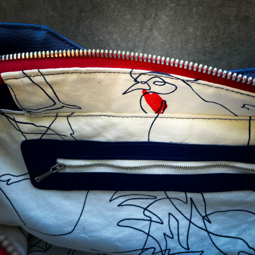 A shoulder bag made with several babywearing wrap coupons (blue, white, and red) and white and blue faux leather.