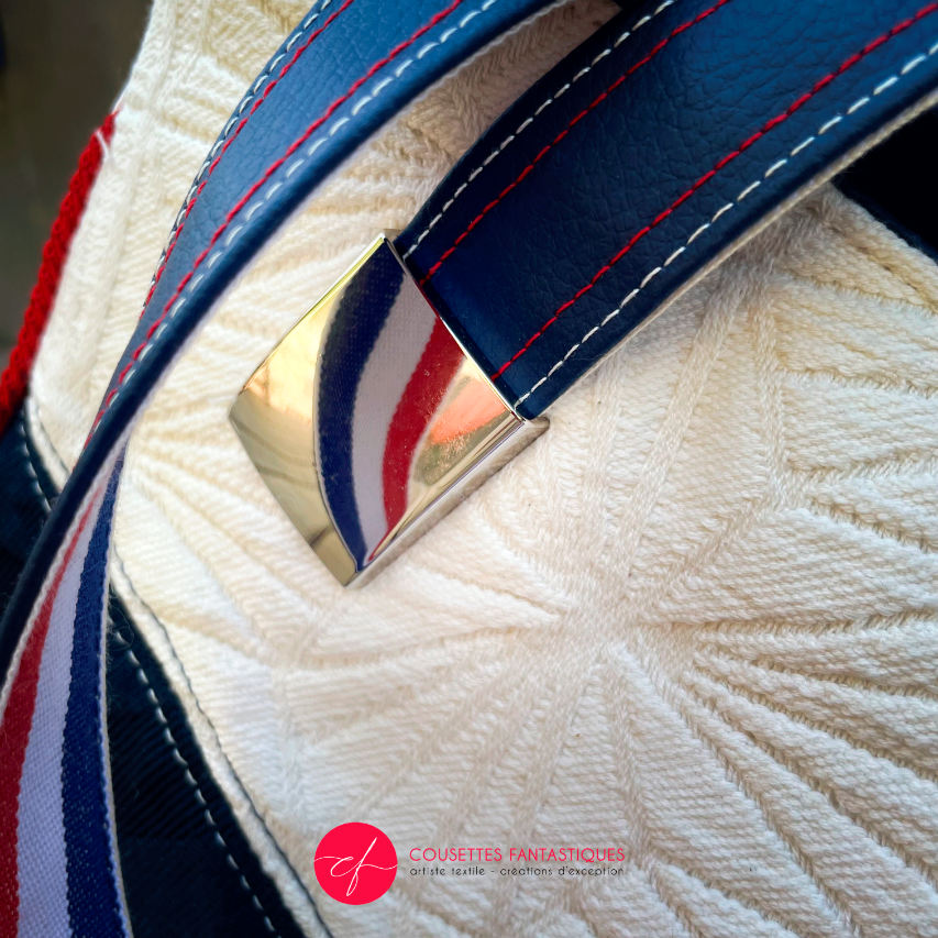 A shoulder bag made with several babywearing wrap coupons (blue, white, and red) and white and blue faux leather.
