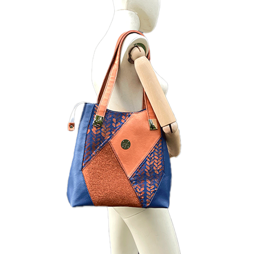 A shoulder bag made up of a patchwork of different materials: royal blue faux leather, golden faux leather, shiny bronze fabric, and blue and bronze wrap fabric with a pattern of small droplets.