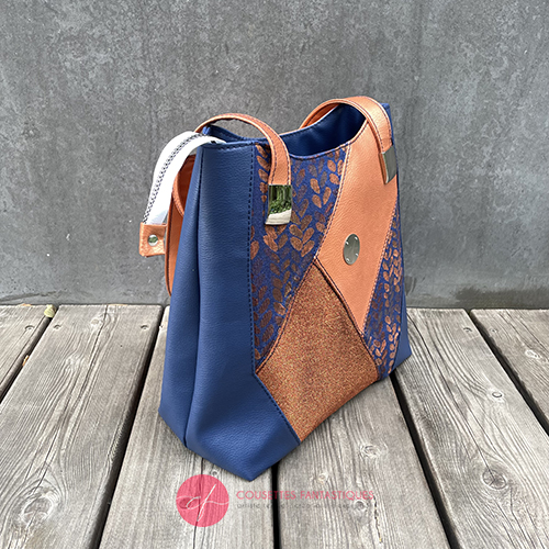 A shoulder bag made up of a patchwork of different materials: royal blue faux leather, golden faux leather, shiny bronze fabric, and blue and bronze wrap fabric with a pattern of small droplets.