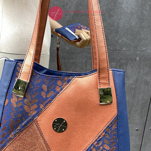 A shoulder bag made up of a patchwork of different materials: royal blue faux leather, golden faux leather, shiny bronze fabric, and blue and bronze wrap fabric with a pattern of small droplets.