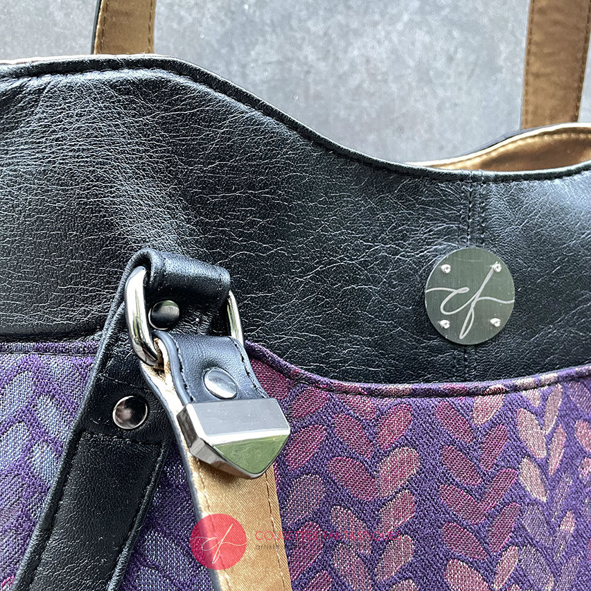 A shoulder bag made from fabric in purples, purples, pinks... with droplet motifs, and upcycled black lamb leather.