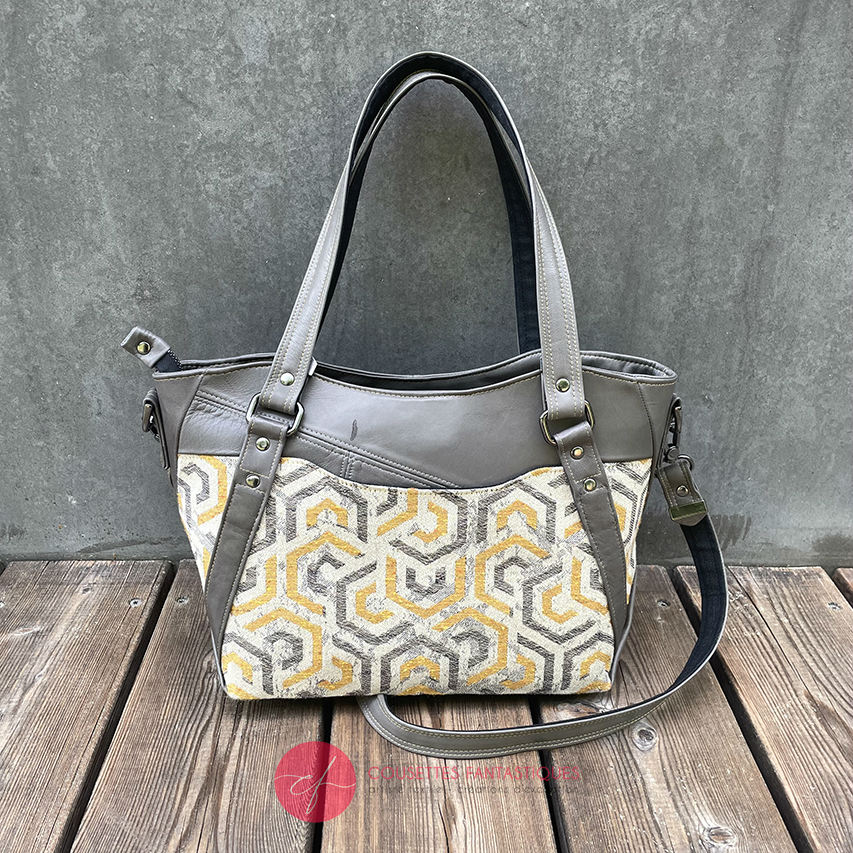 A shoulder bag made from gray, mustard, and ecru babywearing wrap with geometric patterns, and gray lamb leather.