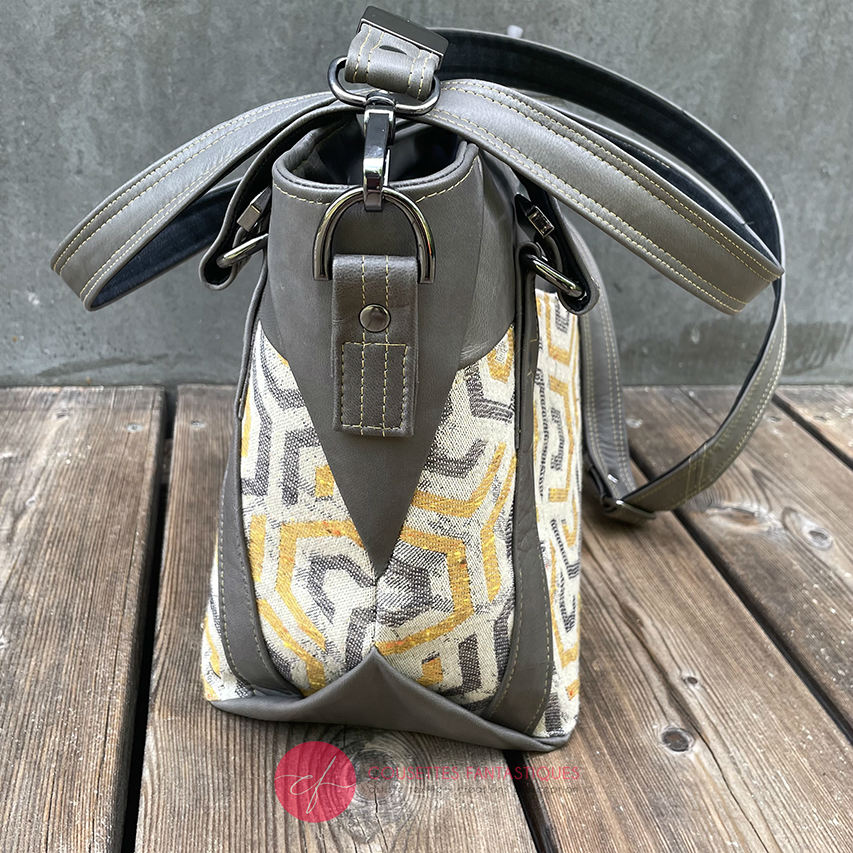 A shoulder bag made from gray, mustard, and ecru babywearing wrap with geometric patterns, and gray lamb leather.