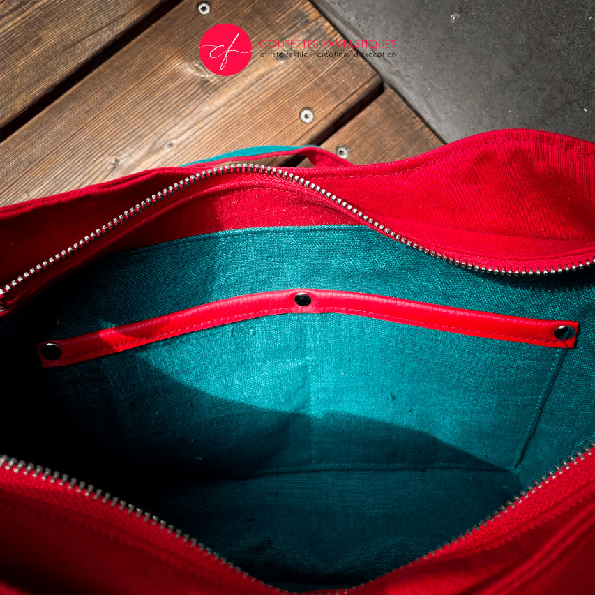 A shoulder bag made from blood red and emerald green babywearing wrap with a thistle pattern, red gabardine, emerald green linen, and synthetic material.