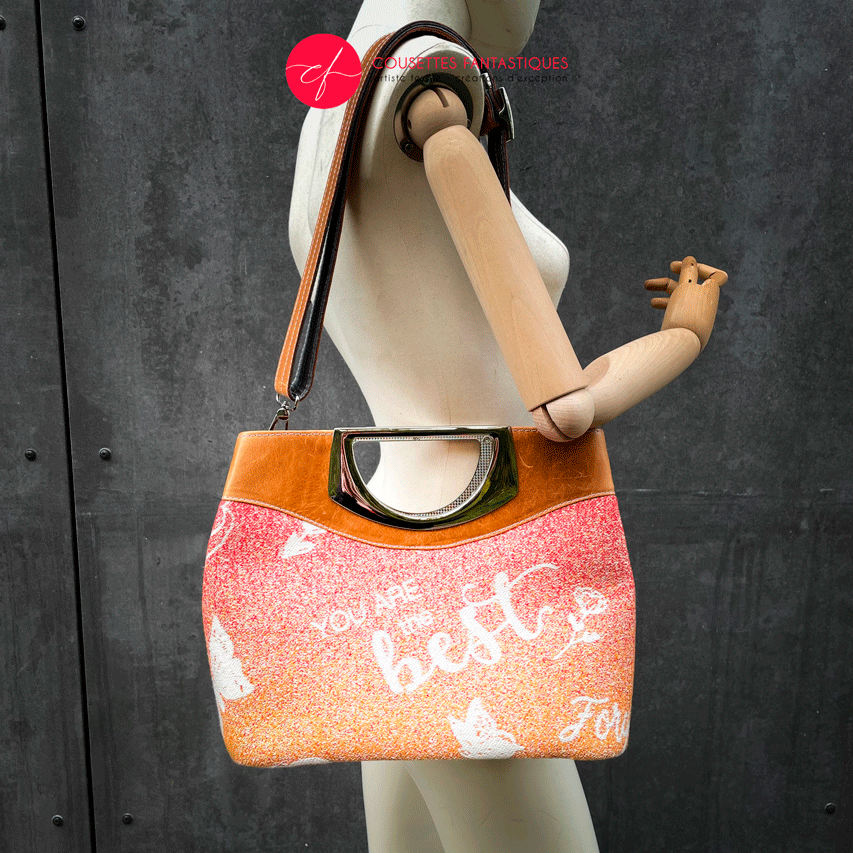 A shoulder bag made of caramel cowhide leather and a gradient-colored babywearing wrap with motivational texts and icons in white.