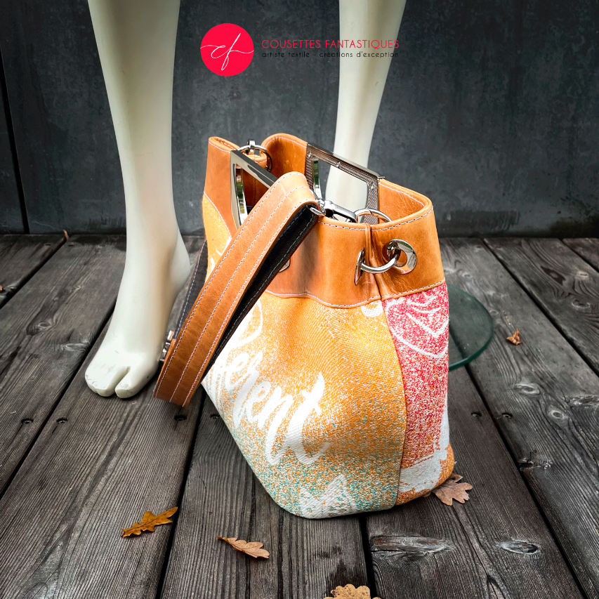 A shoulder bag made of caramel cowhide leather and a gradient-colored babywearing wrap with motivational texts and icons in white.