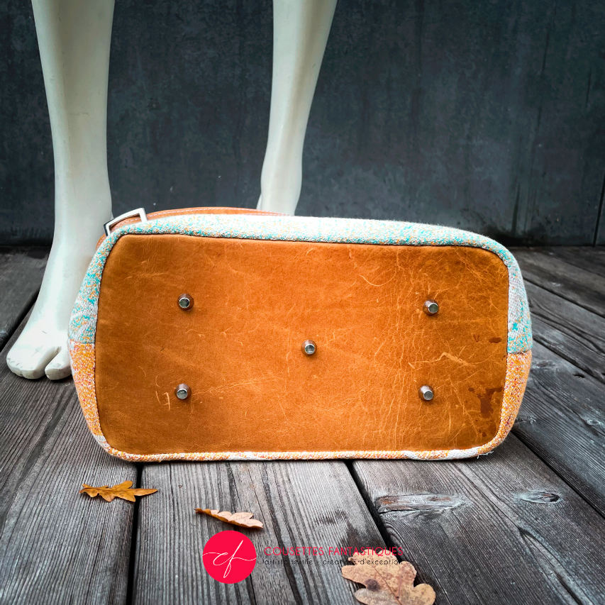 A shoulder bag made of caramel cowhide leather and a gradient-colored babywearing wrap with motivational texts and icons in white.