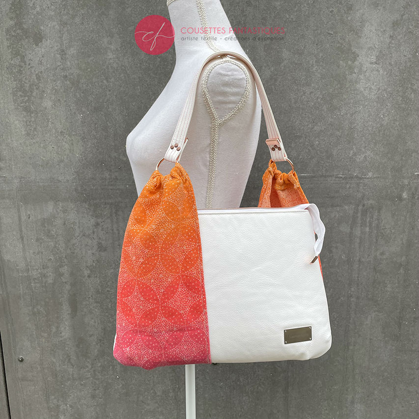 A shoulder bag made from babywearing wrap with a gradient from orange-yellow to pink, with a pointillist star pattern, and white synthetic leather.