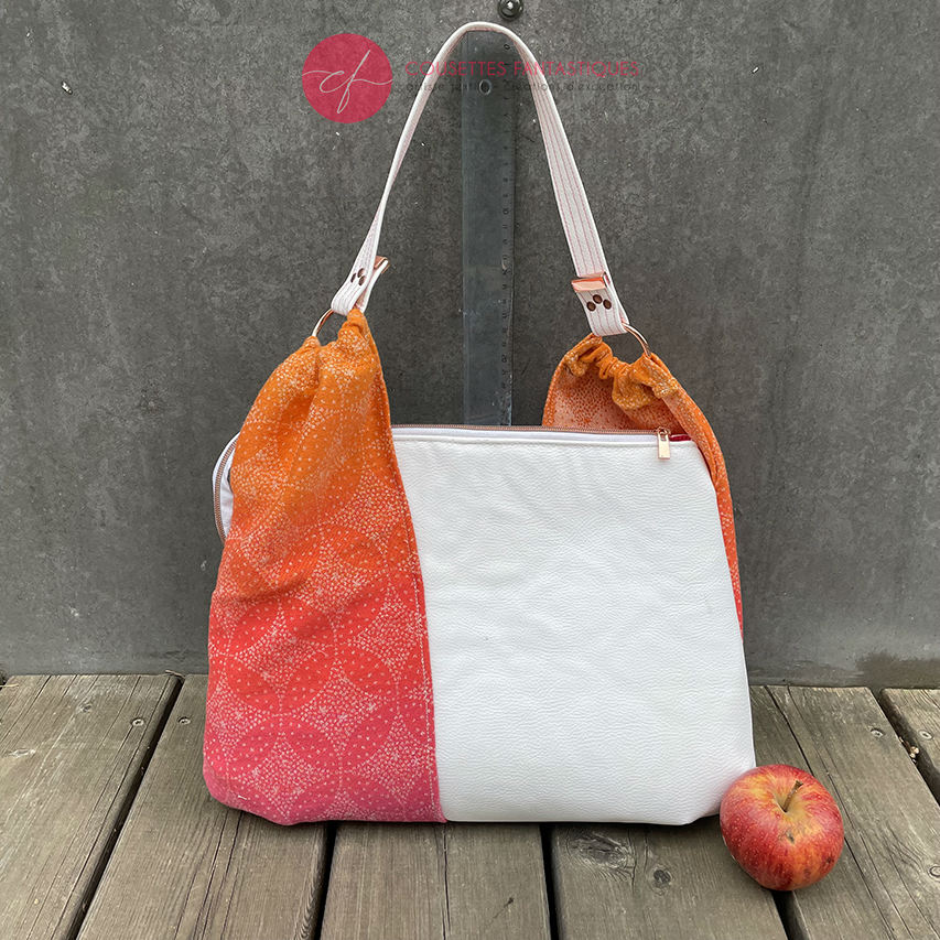 A shoulder bag made from babywearing wrap with a gradient from orange-yellow to pink, with a pointillist star pattern, and white synthetic leather.