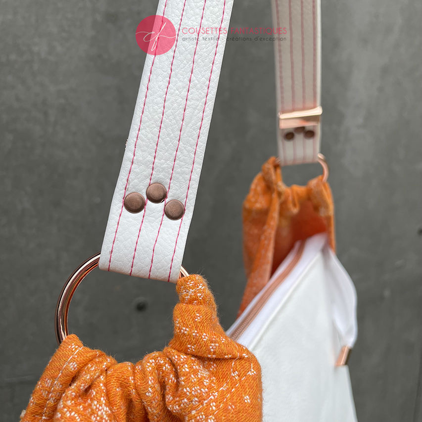 A shoulder bag made from babywearing wrap with a gradient from orange-yellow to pink, with a pointillist star pattern, and white synthetic leather.