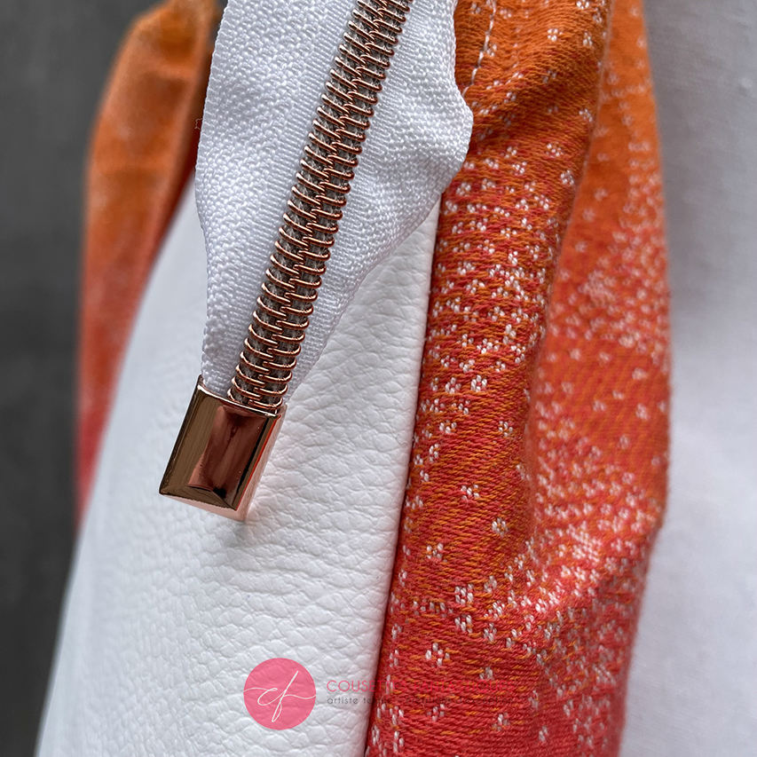 A shoulder bag made from babywearing wrap with a gradient from orange-yellow to pink, with a pointillist star pattern, and white synthetic leather.