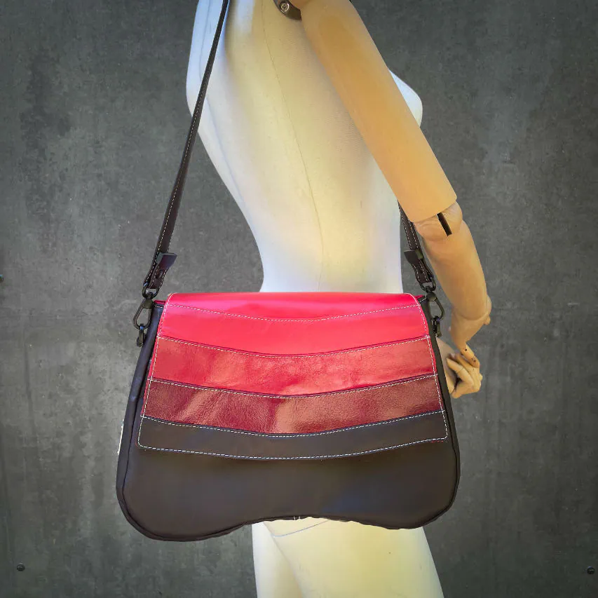 A shoulder bag made of leathers in different shades of red, with brown accents and a red lining.
