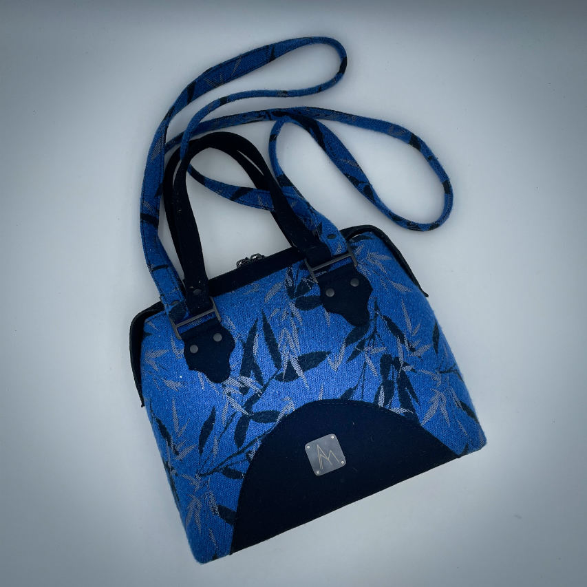 A shoulder bag made from baby wrap fabric featuring a black and royal blue bamboo pattern, paired with boiled black wool and glittered textured leather, complemented by a blue-gray satin lining.