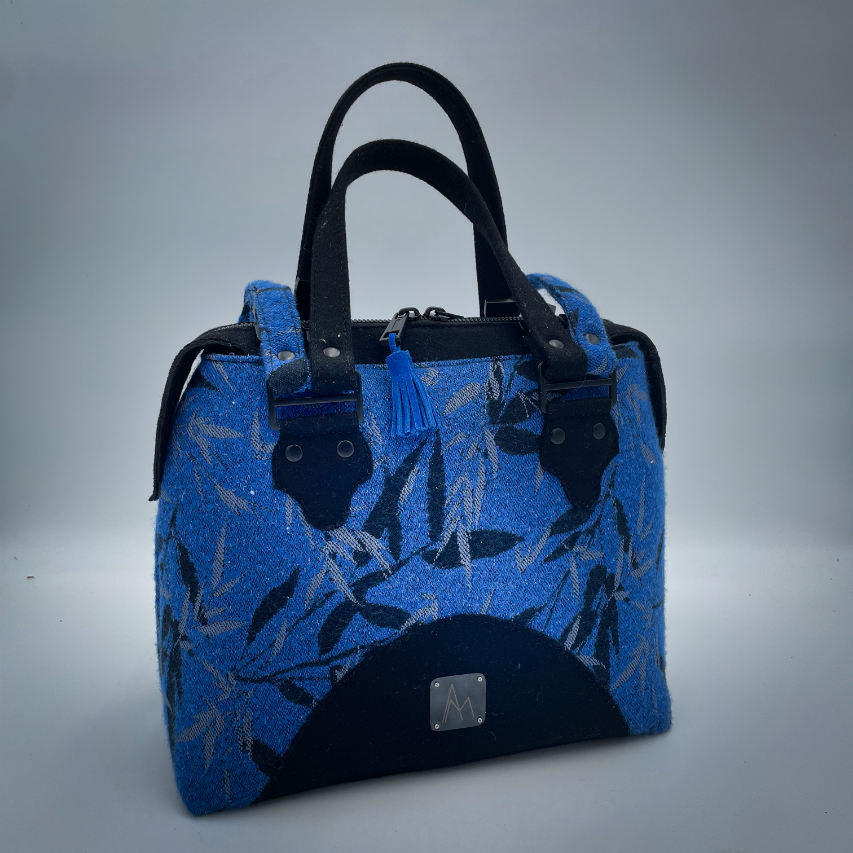 A shoulder bag made from baby wrap fabric featuring a black and royal blue bamboo pattern, paired with boiled black wool and glittered textured leather, complemented by a blue-gray satin lining.