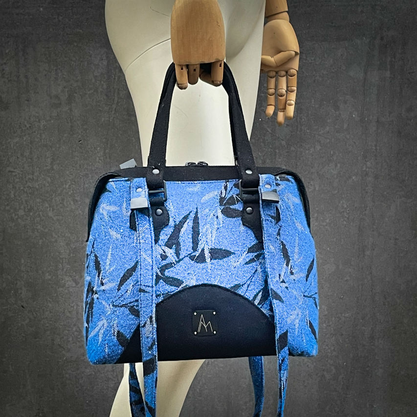 A shoulder bag made from baby wrap fabric featuring a black and royal blue bamboo pattern, paired with boiled black wool and glittered textured leather, complemented by a blue-gray satin lining.