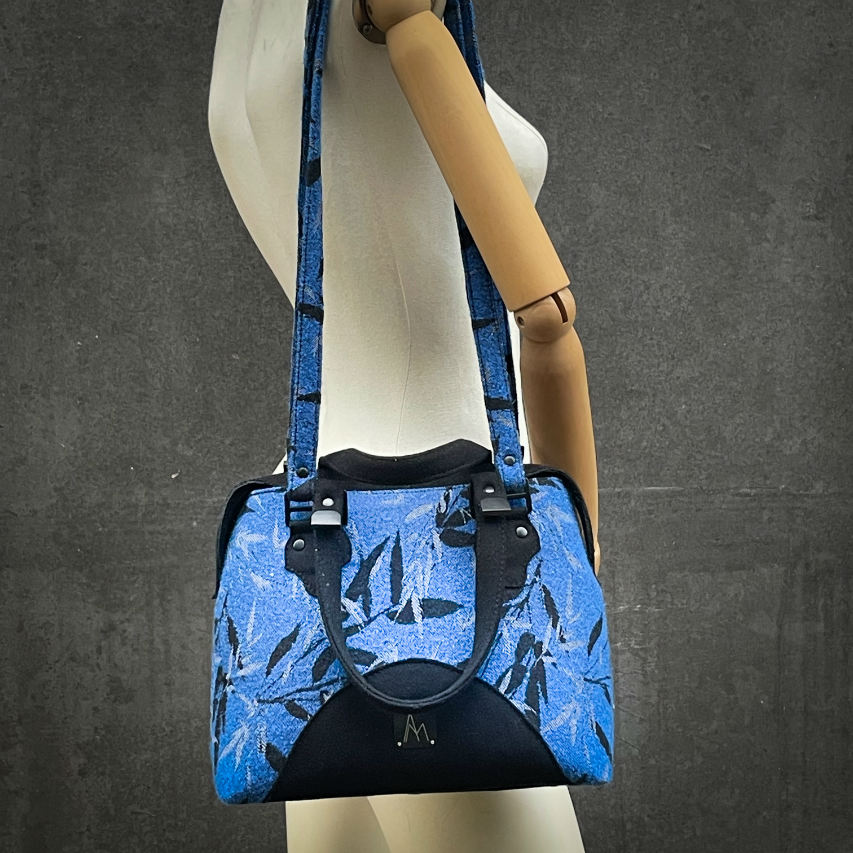 A shoulder bag made from baby wrap fabric featuring a black and royal blue bamboo pattern, paired with boiled black wool and glittered textured leather, complemented by a blue-gray satin lining.