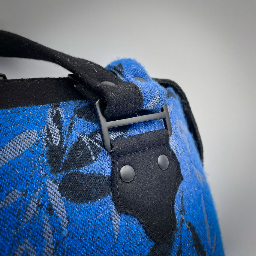 A shoulder bag made from baby wrap fabric featuring a black and royal blue bamboo pattern, paired with boiled black wool and glittered textured leather, complemented by a blue-gray satin lining.