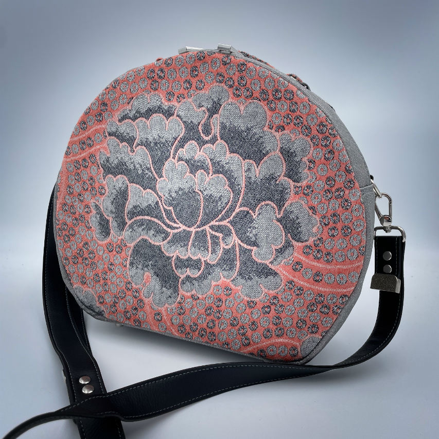 A round shoulder bag made of gray glitter vinyl canvas, with a vintage floral patterned pink and gray baby sling scrap and a gray satin lining.