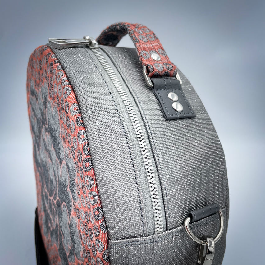 A round shoulder bag made of gray glitter vinyl canvas, with a vintage floral patterned pink and gray baby sling scrap and a gray satin lining.