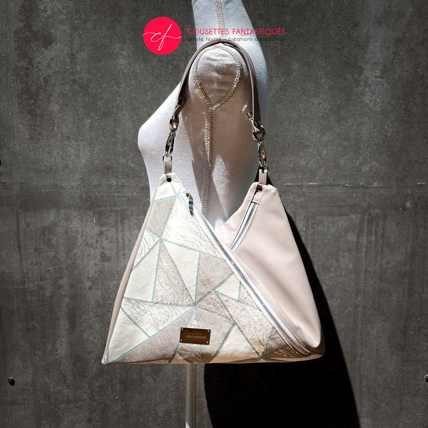 A triangular shoulder bag made of beige synthetic leather and white, cream, beige, and green babywearing fabric.